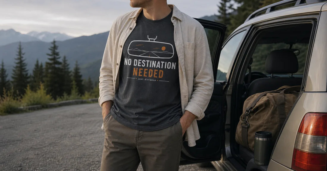 Traveler wearing a road-themed graphic T-shirt beside a packed vehicle at a quiet mountain roadside stop.